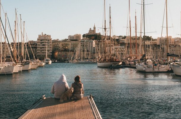A man and woman sit on a dock with a dog, enjoying a peaceful moment by the water.