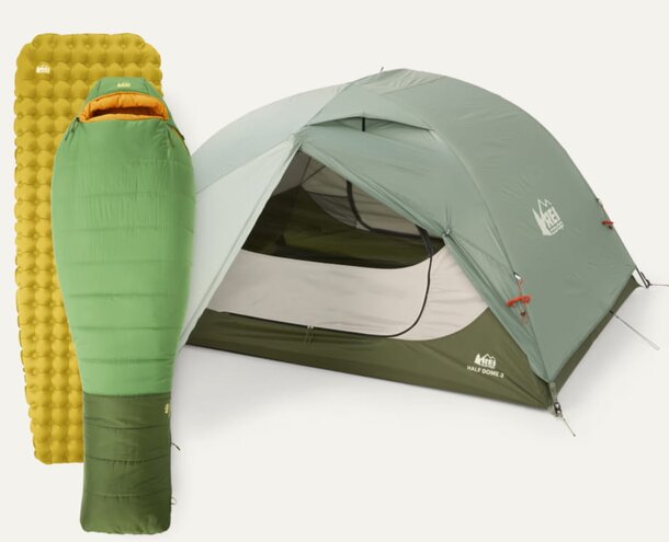 A green-covered tent set up beside a sleeping pad, ready for camping in a natural outdoor setting.