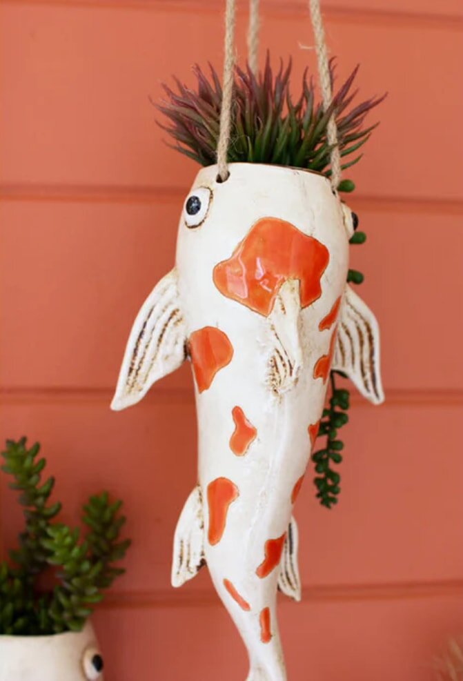 A ceramic fish planter is mounted on a wall, featuring vibrant colors and a whimsical design for decorative plant display.