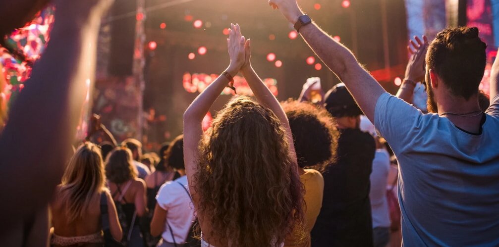 A lively crowd at a music festival, with many people raising their hands in excitement and enjoyment.