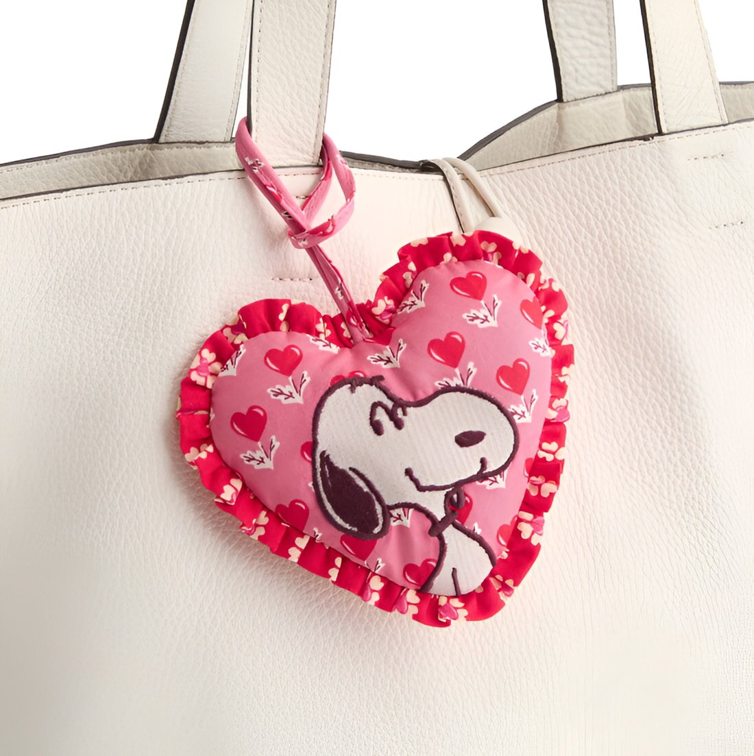 A white leather bag features a pink heart-shaped decoration with a black-and-white cartoon dog print. The heart is adorned with red hearts and ruffled edges.
