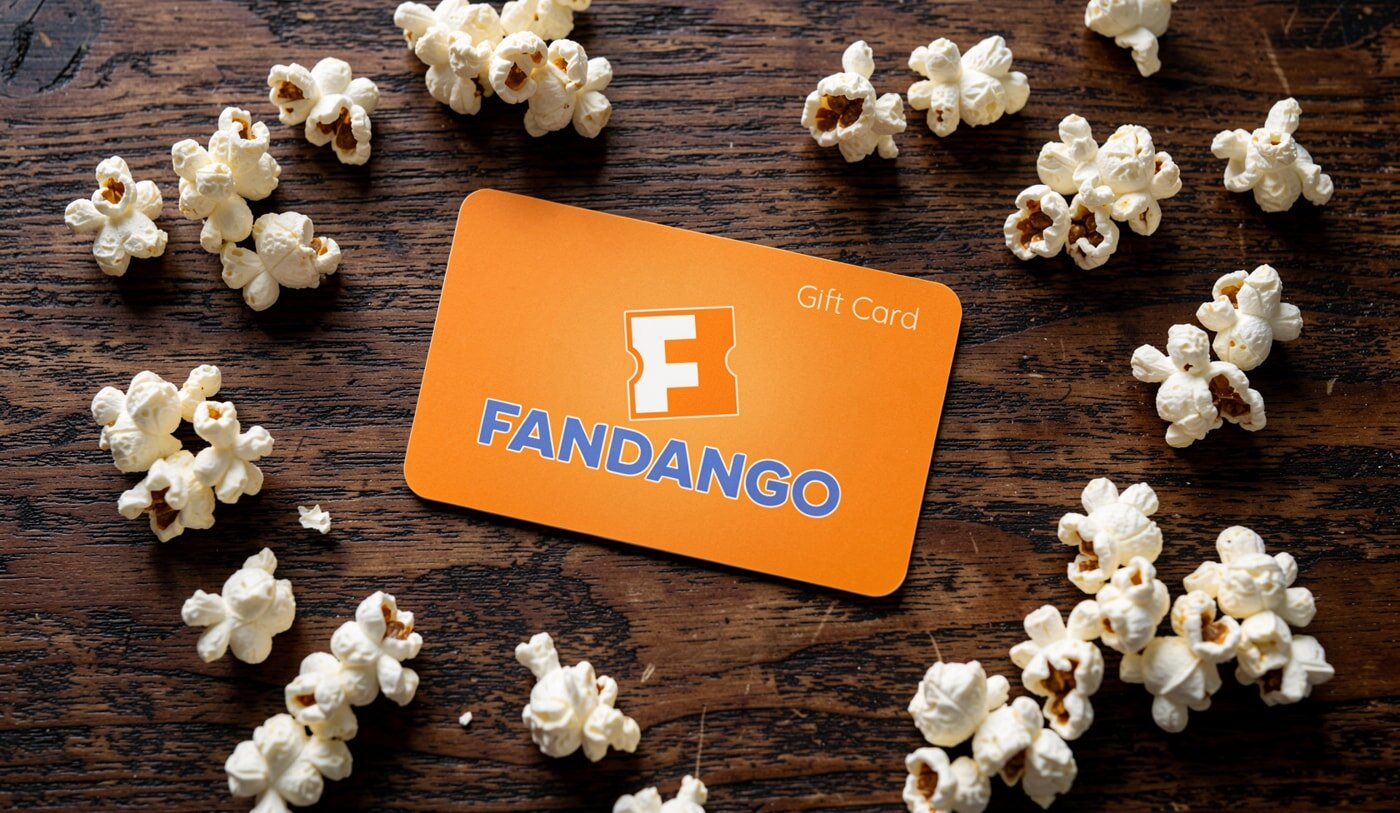 An orange Fandango gift card on a wooden table is surrounded by scattered popcorn, evoking a cinematic and inviting atmosphere.