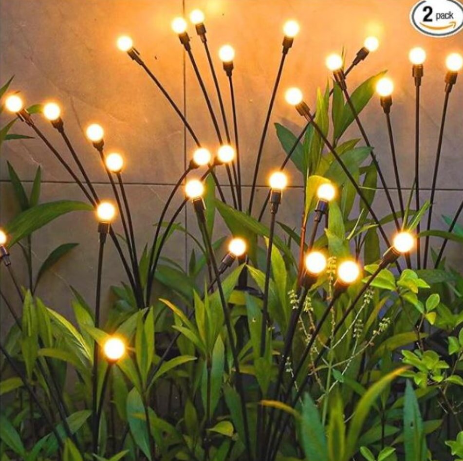 Outdoor garden with glowing lights on tall, slender stems among lush green leaves. The warm bulbs create a serene and inviting atmosphere.