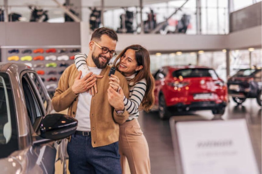 A couple embraces warmly in a modern car showroom, surrounded by sleek vehicles on display.