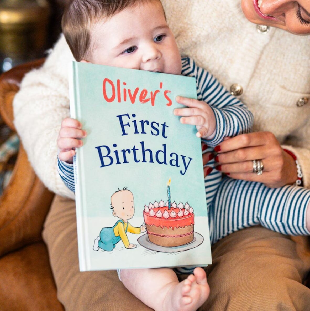 A woman holds a baby while presenting a book celebrating the baby's first birthday.