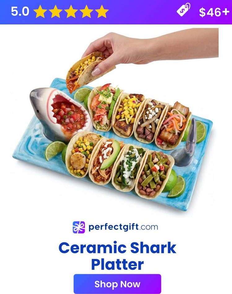 A hand picks a taco from a shark-shaped holder filled with various tacos on a blue tray, surrounded by lime slices.