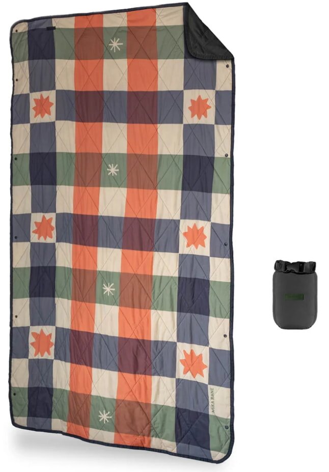 Quilted blanket with a colorful plaid design of blue, orange, green, and white squares, featuring stars and flower patterns; small gray storage bag nearby.