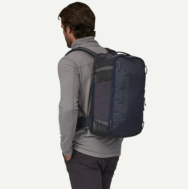 A man seen from behind, wearing a backpack, walking away from the viewer in an outdoor setting.