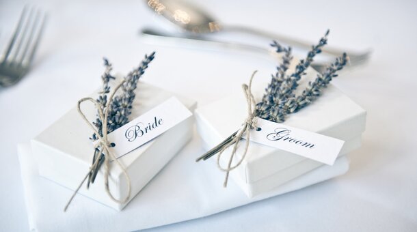 A young woman smiles warmly at an elderly woman in a wheelchair. They hold hands in a comforting, joyful interaction. The room is softly lit and homey.