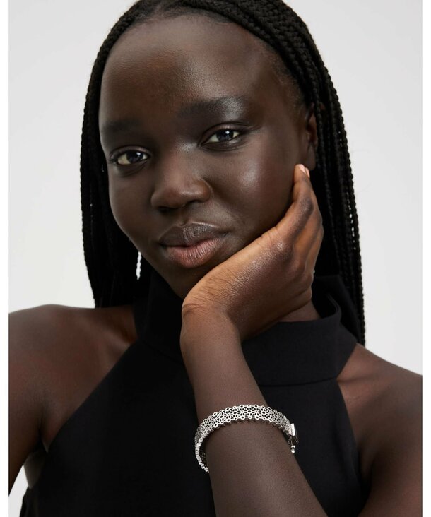 A woman with braids dressed in a sleek black dress poses gracefully, highlighting her fashion choice.