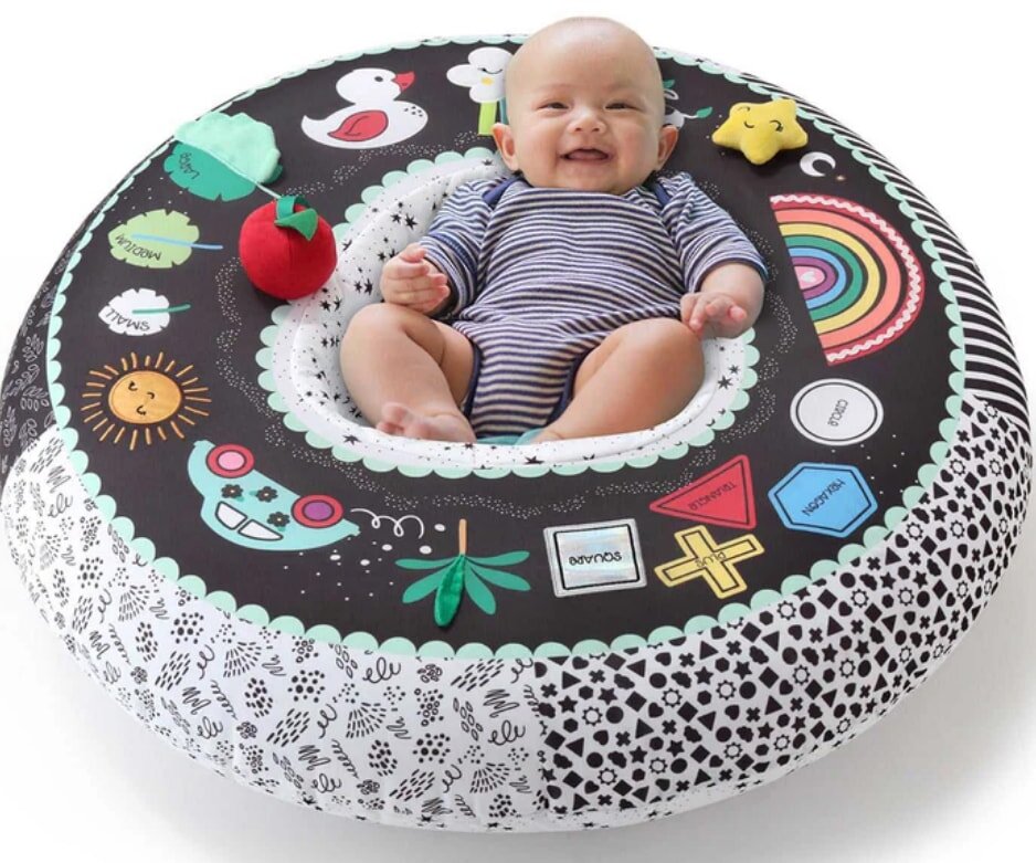 A baby sits in a round seat surrounded by colorful toys, engaging with the playful environment.