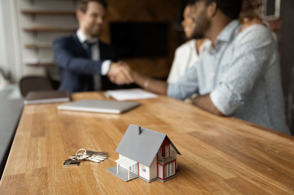 Model house and keys on a table with people shaking hands