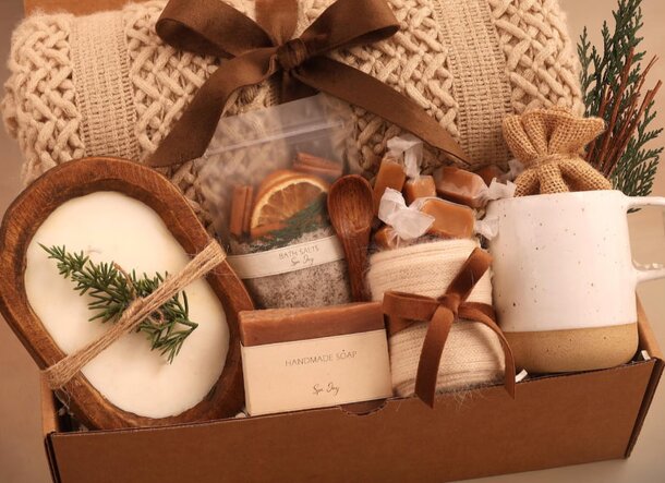 A cozy box containing a soft blanket, lit candles, and a steaming mug, creating a warm and inviting atmosphere.