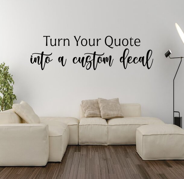 A modern living room with a cream sofa and cushions, a green plant, and a tall floor lamp. Text on the wall reads, "Turn Your Quote into a custom decal."