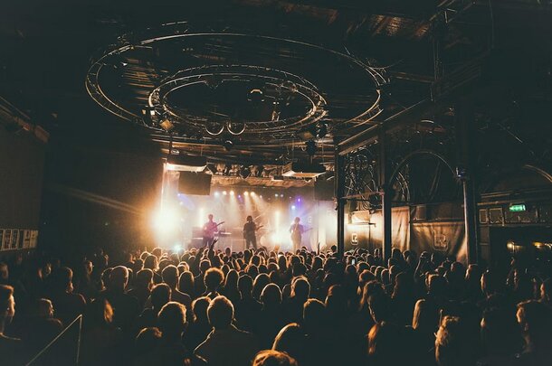 A lively crowd in a dimly lit room, focused on a band playing music on stage.
