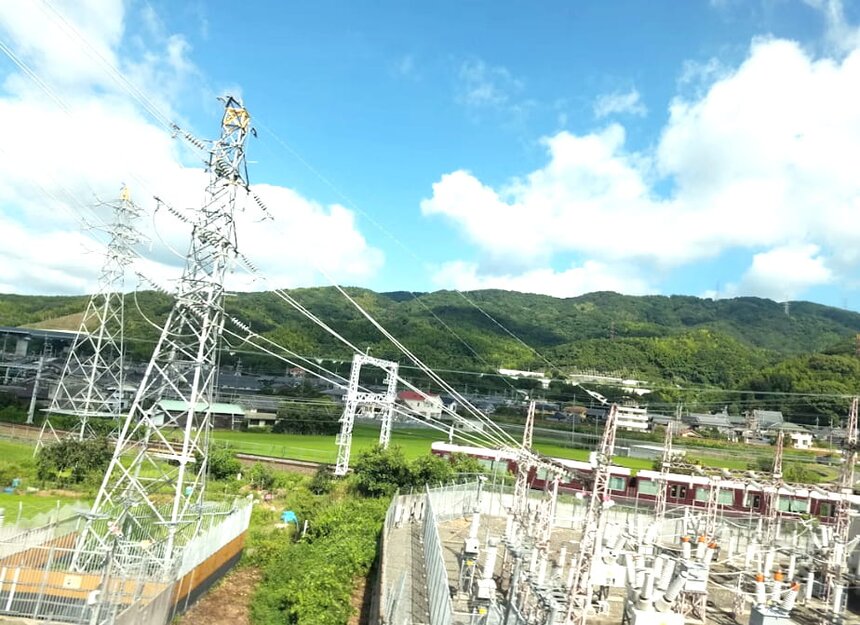 A power plant with tall smokestacks and high voltage lines stretching across the landscape under a clear blue sky.
