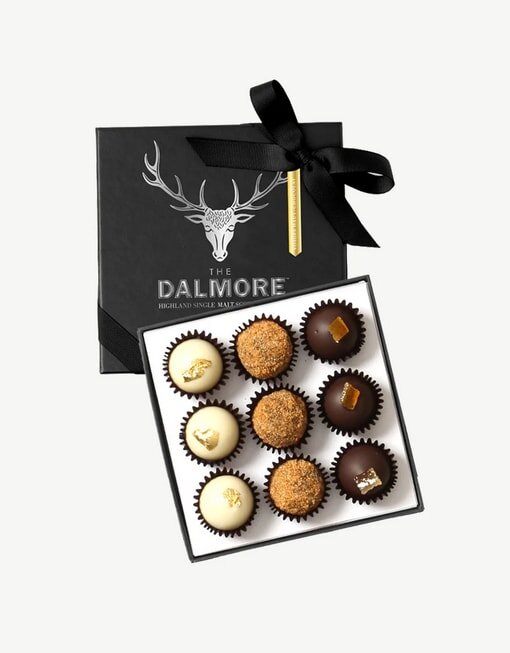 A Dalmore-branded box with nine assorted chocolates, elegantly arranged, featuring a black ribbon and stag logo on the lid.