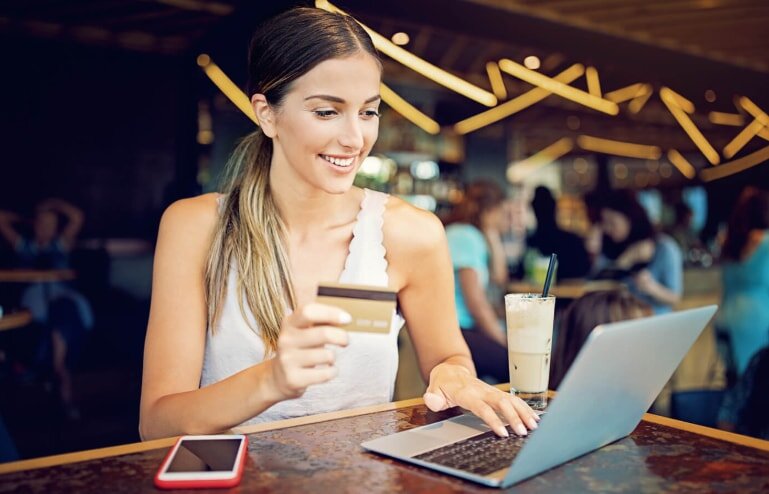 A woman holds a credit card while using her laptop, focused on an online transaction.