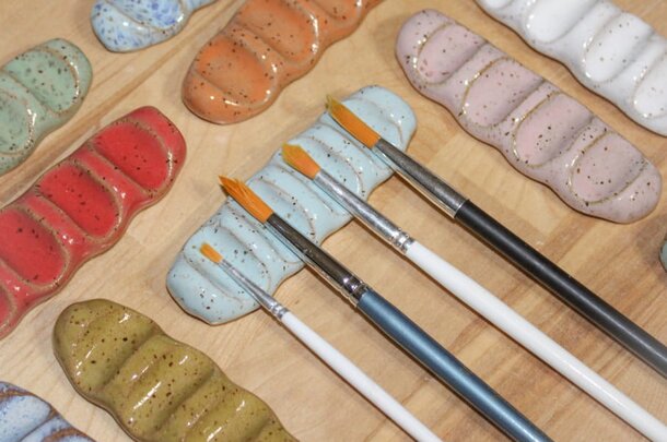 Ceramic paint brushes and paintbrushes arranged on a wooden table, showcasing their vibrant colors and varied sizes.