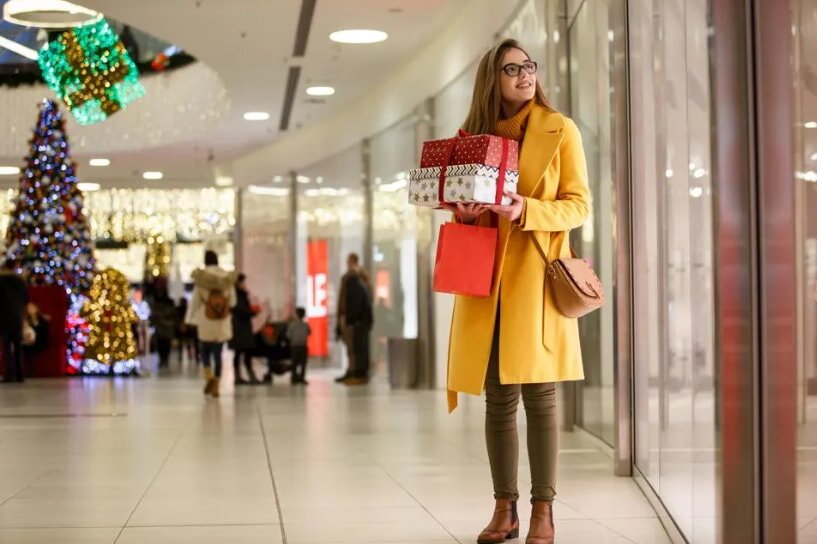 A woman in a bright yellow coat is holding a shopping bag while standing outdoors.