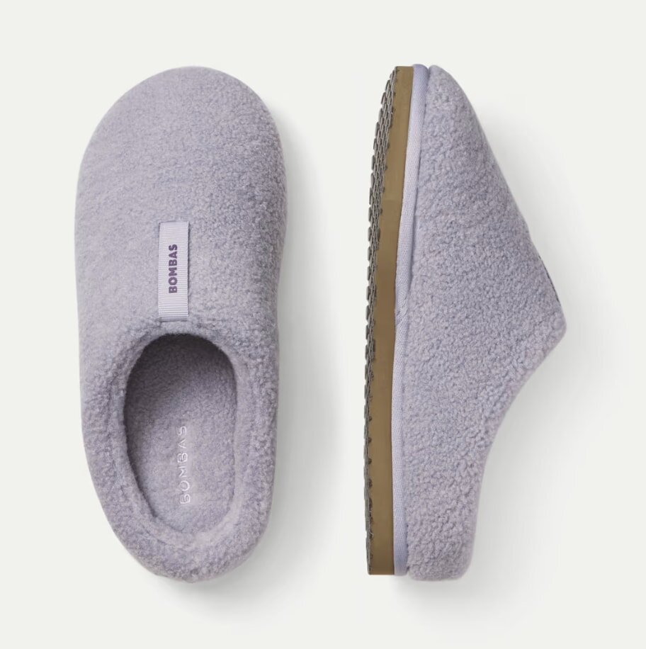 Cozy gray slippers with soft, textured material and rubber soles. One slipper is shown from above, and the other from the side, displaying the brand name.