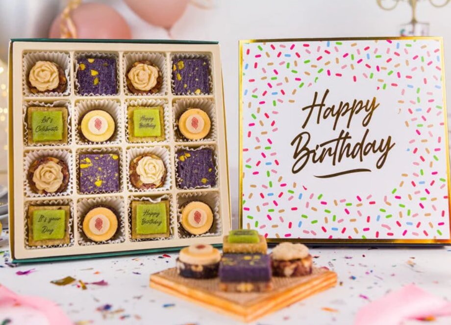 A box of assorted chocolates next to a colorful birthday card, suggesting a gift for a celebration.