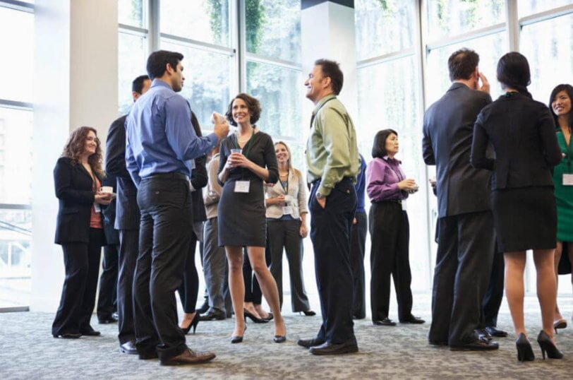 A group of business professionals engaged in discussion around a conference table in a modern meeting room.