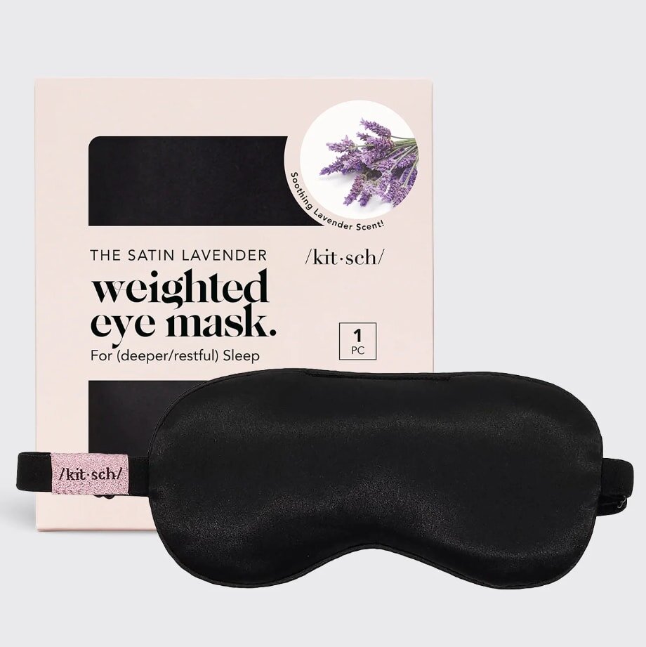 Black satin weighted eye mask in front of a beige box with the text "The Satin Lavender Weighted Eye Mask." A lavender sprig image highlights its soothing scent.