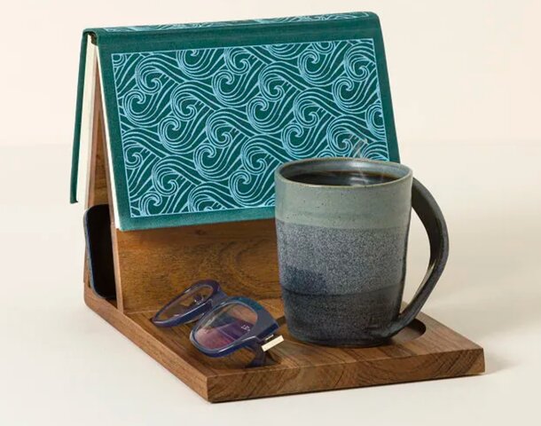 A book and a coffee cup resting on a wooden tray, creating a cozy reading atmosphere.