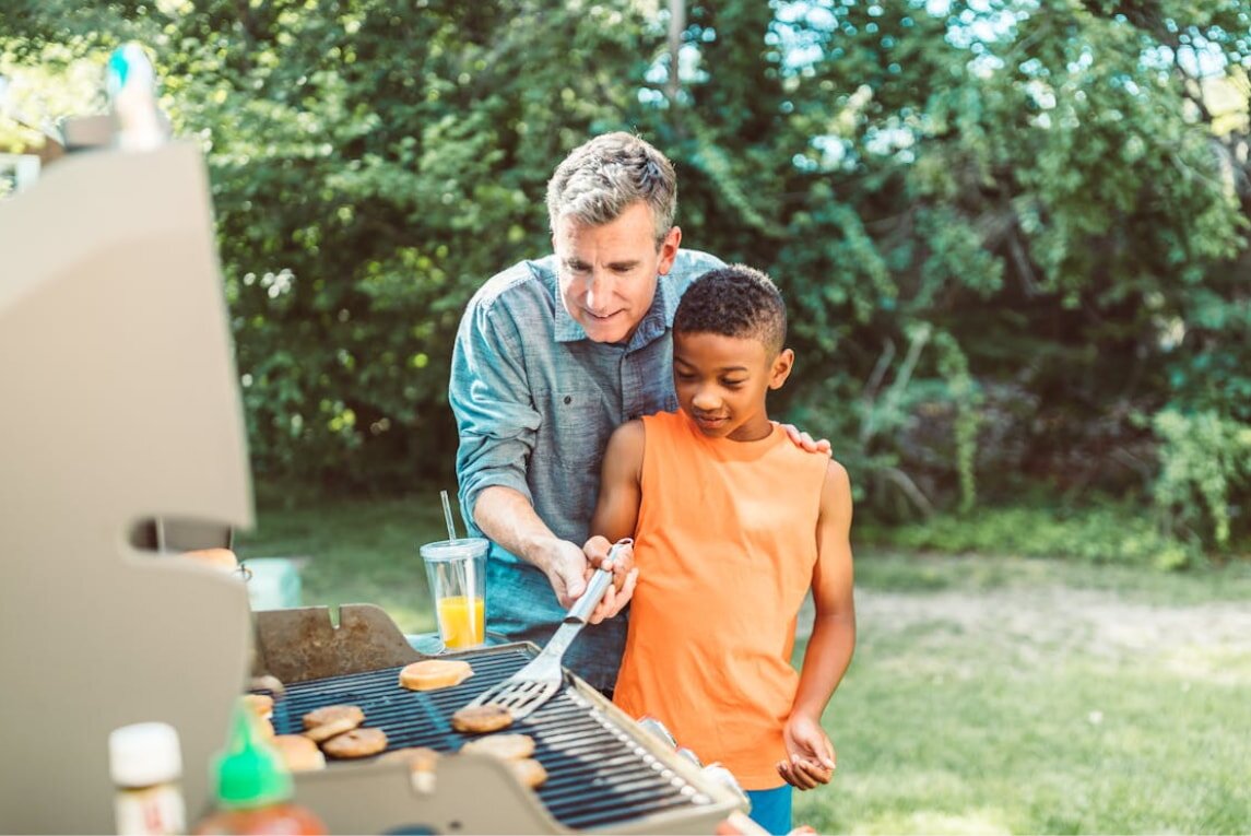 A father and son happily cooking together at a grill, enjoying quality time outdoors.