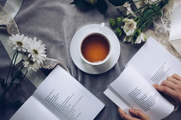 A cup of tea beside an open book on a table adorned with colorful flowers.