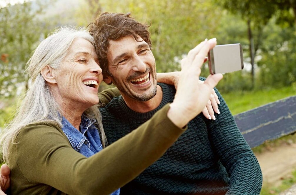 A man and woman smiling together while taking a selfie outdoors.