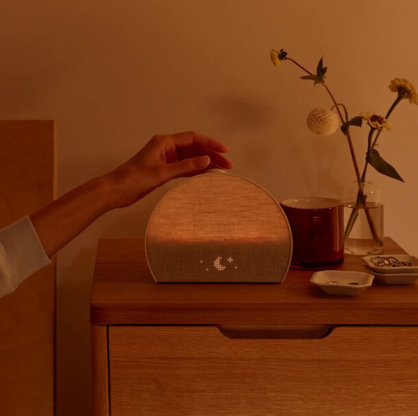 A person sets a lamp on a nightstand, preparing the space for reading or relaxation.