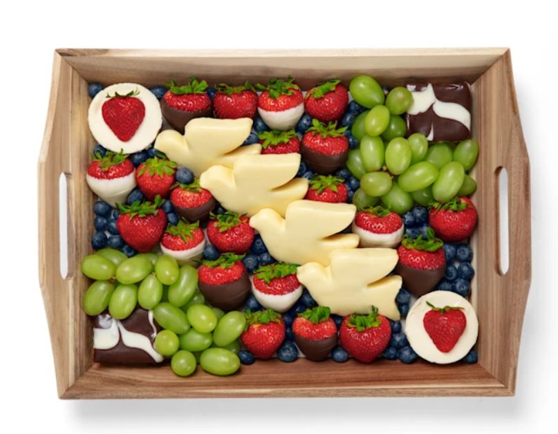 A wooden tray filled with assorted fruits and various types of cheese, arranged attractively for serving.
