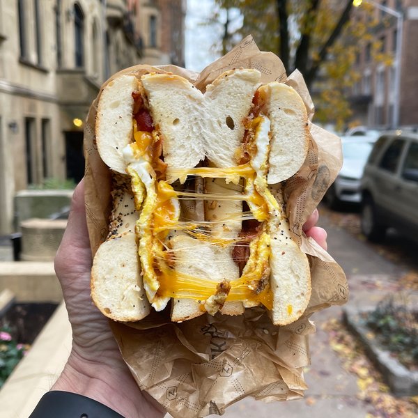 Decadent bacon, egg and cheese on a bagel, split open and held aloft.