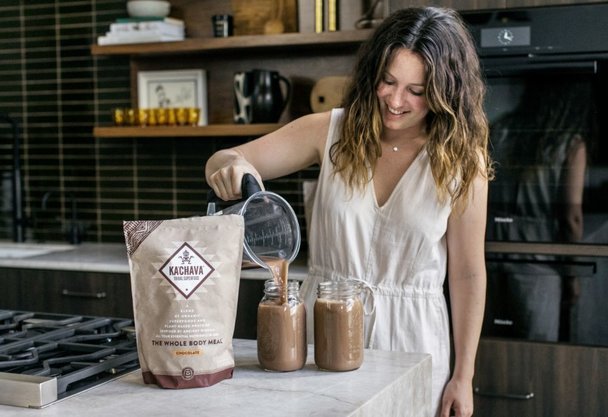 Woman smiling in her kitchen, preparing two chocolate Ka'Chava shakes.