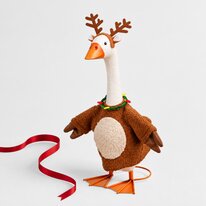 Porch goose dressed as a reindeer in a brown fuzzy costume with antlers and a festive collar, posed beside a red ribbon.