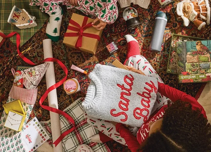 Animated holiday scenes featuring Christmas gift wrapping, festive pajamas, beauty gifts, cozy accessories, toys, plush animals, holiday home décor, decorative geese and two women exchanging jewelry gifts.