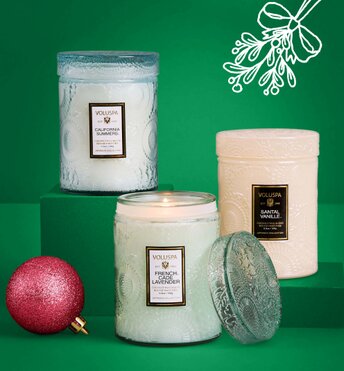 Three candles displayed next to Christmas tree ornaments in front of a green background