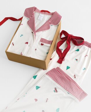 White holiday pajamas with red striped trim and tiny festive motifs, displayed in a gift box with a coordinating pajama top.