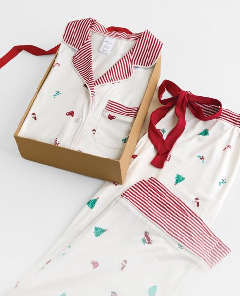 White holiday pajamas with red striped trim and tiny festive motifs, displayed in a gift box with a coordinating pajama top.