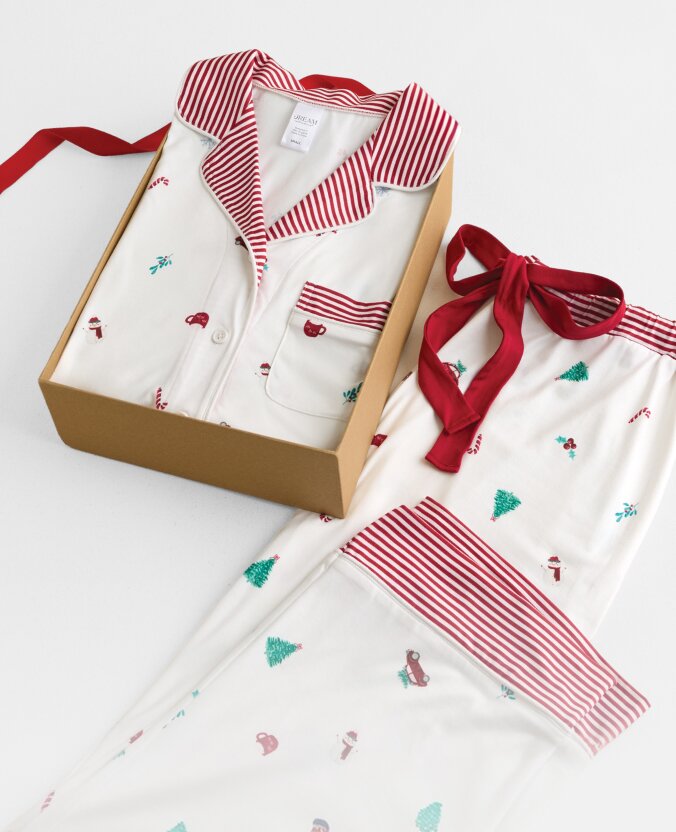 White holiday pajamas with red striped trim and tiny festive motifs, displayed in a gift box with a coordinating pajama top.