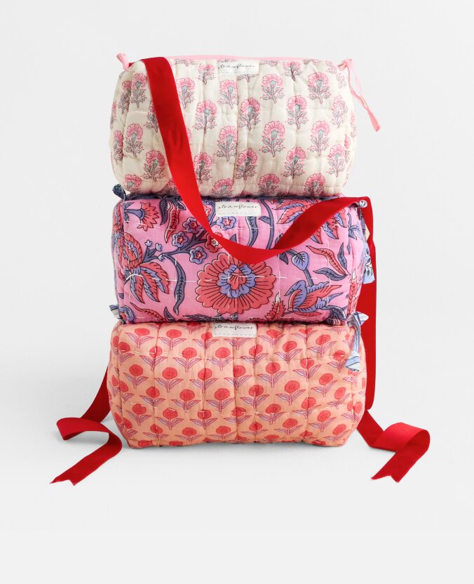 Three stacked Strawflower cosmetic bags in pink and coral patterns, finished with red ribbon handles and bows