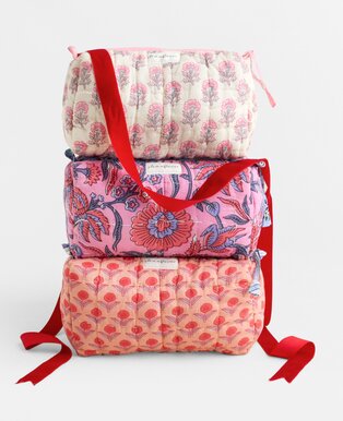 Three stacked Strawflower cosmetic bags in pink and coral patterns, finished with red ribbon handles and bows