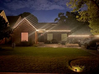 Brick home at dusk with warm white lights along the roofline and porch