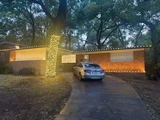 Ranch home with roofline lights, a lit spiral tree, and a car in the driveway