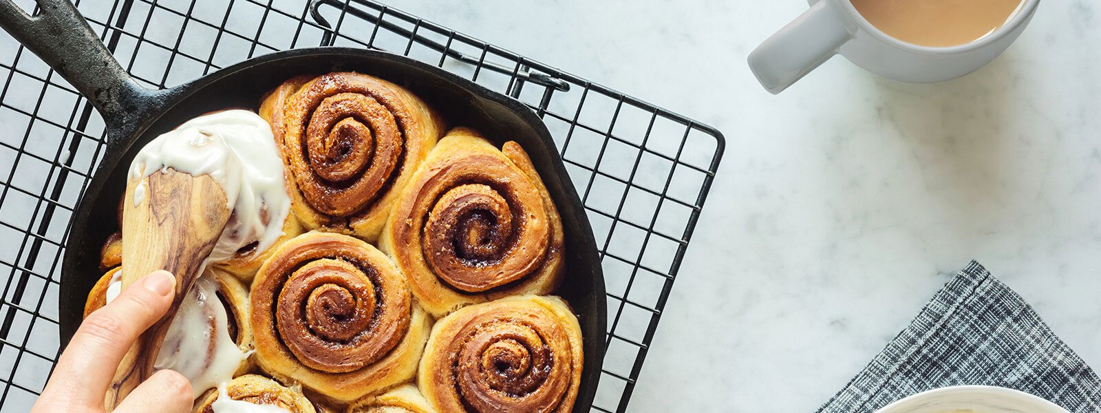 Freshly baked cinnamon buns are being iced in a cast iron pan. 