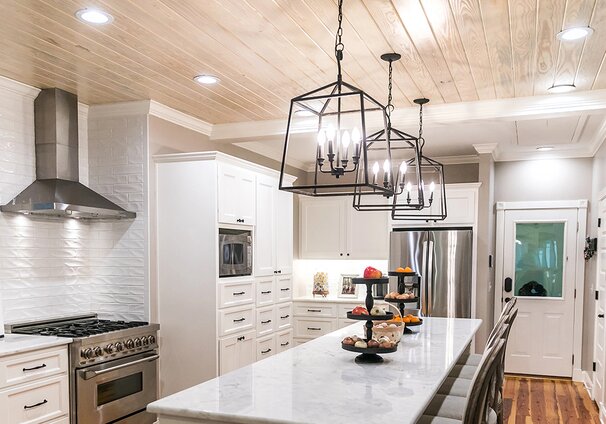 A bright kitchen with potlights and three chandeliers over the island.