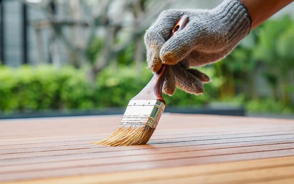 A painter uses a brush to stain wooden planks.