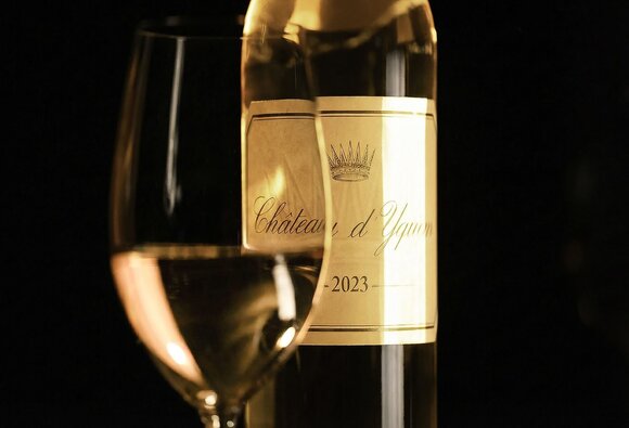 Glass of white wine beside a bottle of Château d'Yquem 2023 against a dark background